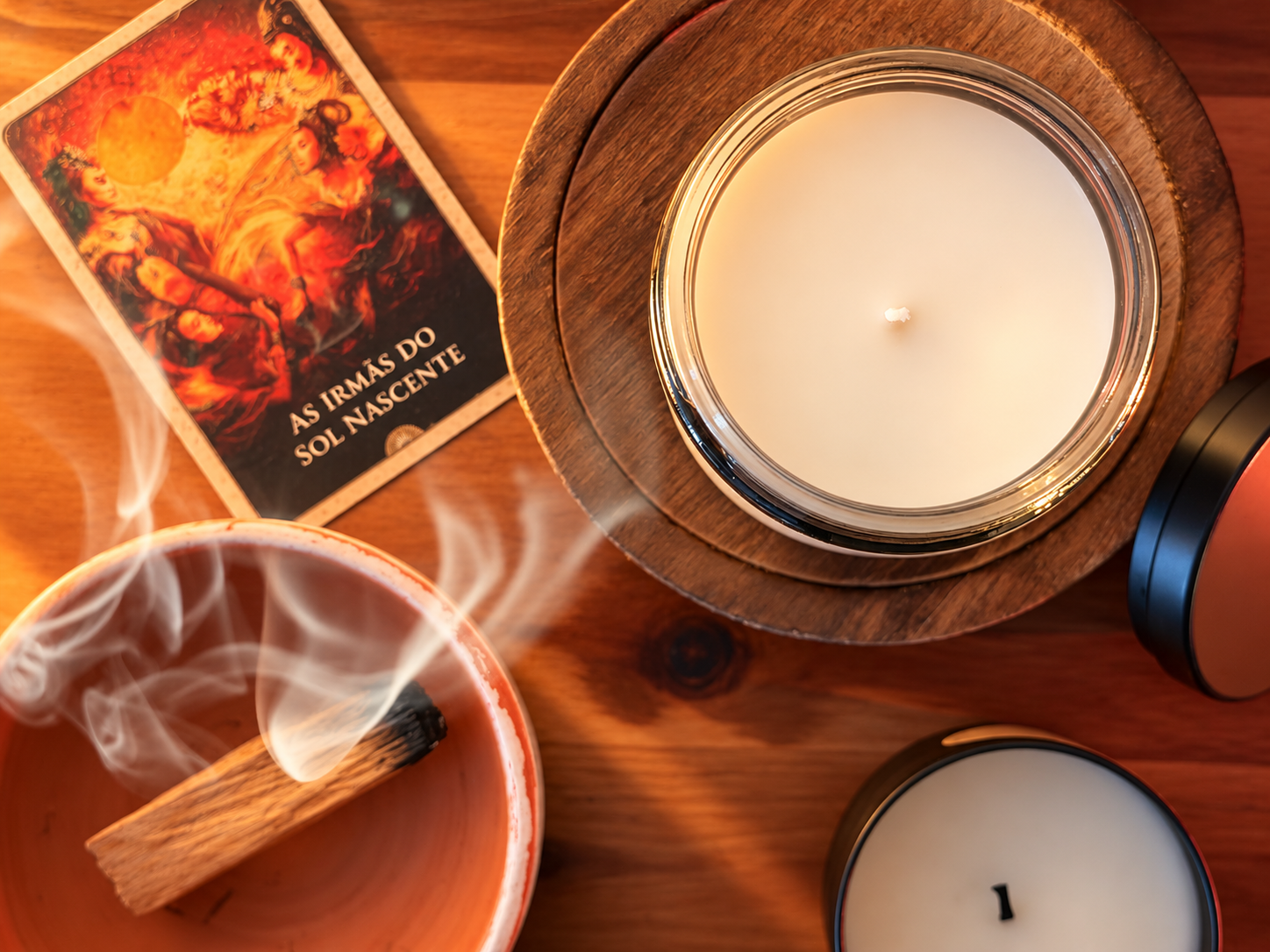 An unlit candle with palo santo smoke and an oracle card on a warm wooden table